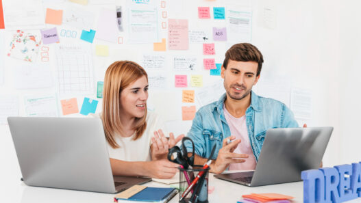 A man and woman seated at a desk with laptops, illustrating partnership in transforming brands through web design expertise.