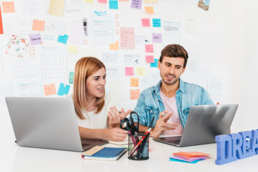 A man and woman seated at a desk with laptops, illustrating partnership in transforming brands through web design expertise.