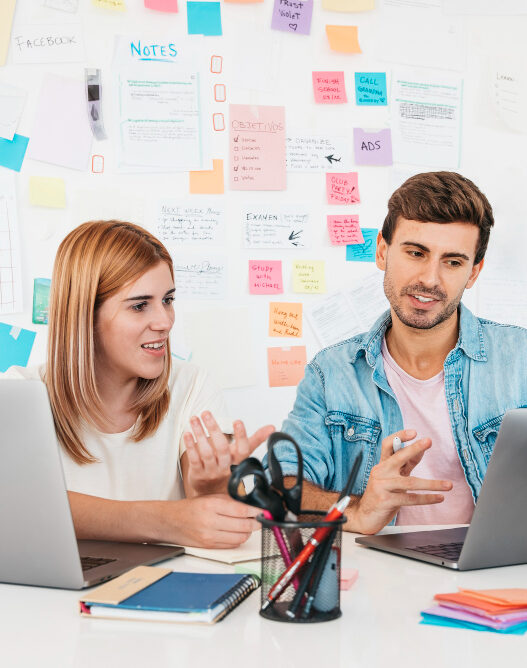 A man and woman seated at a desk with laptops, illustrating partnership in transforming brands through web design expertise.